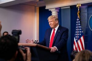 Donald Trump hablando en el podio de la Casa Blanca con banderas estadounidenses, comentando sobre Venezuela