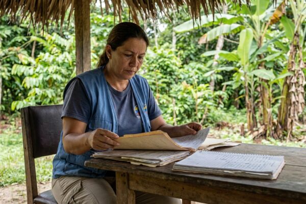 Trabajador de salud pública venezolano revisando documentos médicos en zona rural tropical con vegetación selvática